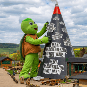 Ein KI erstelltes Foto, auf dem unser überdimensional großes Maskottchen Hildi die Riesenräucherkerze mit vielen Aufklebern: MAKE RAACHERKERZLN; NOT WAR! beklebt.